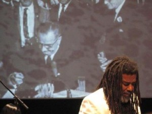 Wadada_Leo_Smith_in_front_of_projection_of_LBJ_signing_Voting_Rights_Act__1964_Ten_Freedom_Summers__October__2011_copyright_2011_Lyn_Horton_depth1